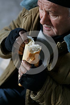 Depressed senior-aged beggar eating bread