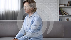 Depressed senior lady sitting on couch, feeling anxious, psychological problems