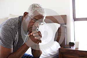 Depressed Senior Man Looking Unhappy Sitting On Side Of Bed At Home With Head In Hands