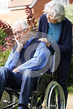 Depressed Senior Man In Wheelchair Being Pushed By Wife photo