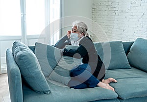 Depressed senior widow woman with protective mask alone at home feeling sad and missing family