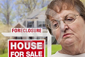 Depressed Senior Woman in Front of Foreclosure Real Estate Sign photo