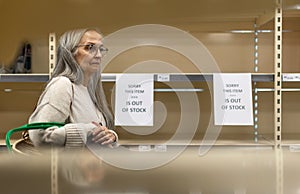 Depressed senior woman shopper in front of empty shelves in a grocery store