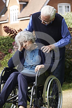 Depressed Senior Woman In Wheelchair Being Pushed By Husband