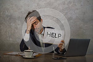 Depressed and stressed attractive hispanic man in suit and tie working overwhelmed office computer desk holding notepad asking for