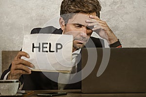 Depressed and stressed attractive hispanic man in suit and tie working overwhelmed office computer desk holding notepad asking for