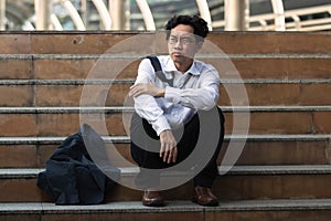 Depressed stressed young Asian business man in suit with hands on head sitting on stairs. Unemployment and layoff concept