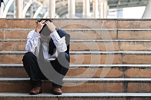 Depressed stressed young Asian business man in suit with hands on head sitting on stairs. Unemployment and layoff concept