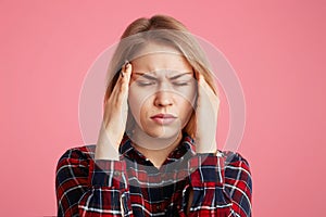 Depressed stressful female has headache, keeps hands on temples, closes eyes as feel terrible pain, being overworked and fatigue, photo