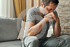 Depressed sulking man sitting alone at living room sofa and thinking