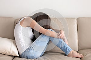 Depressed teen sitting on sofa and embracing knees