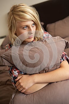 Depressed Teenage Girl Hugging Pillow In Bedroom