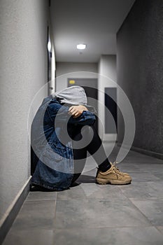 A depressed teenage girl sits alone on the floor in a dark room.