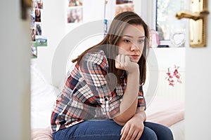 Depressed Teenage Girl Sitting In Bedroom