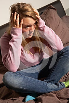 Depressed Teenage Girl Sitting In Bedroom At Home