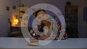 Depressed teenager celebrating birthday, looking at cake with candle, outsider