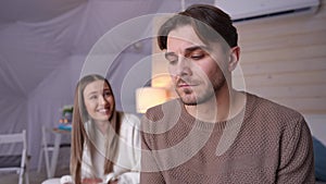 Depressed thoughtful handsome man looking away sighing as blurred woman shouting pushing guy sitting on bed at