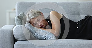 Depressed unhappy mature woman lying on side on home sofa