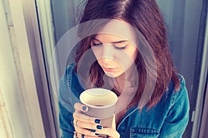 Depressed unhappy young woman sitting on stairs outdoors with coffee