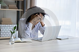 Depressed upset black female sit at workplace hug head