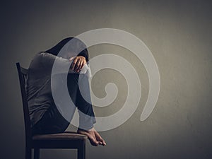 Depressed woman sitting on a chair in dark room at home.