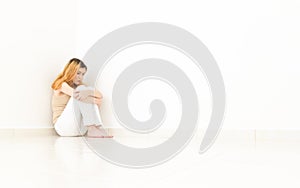 Depressed woman sitting in the corner of the room. The walls are photo