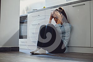 Depressed woman sitting on a kitchen floor