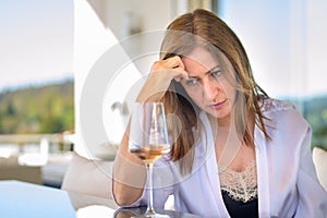 Depressed woman sitting thinking deeply with a glass of red wine