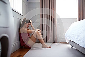 Depressed Woman Wearing Pajamas Sitting On Floor Of Bedroom