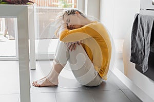 Depressed 30 years woman sitting on kitchen floor with hugging knees. Loneliness, sadness. Mental health, drug abuse and