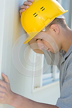 Depressed young builder holding head against wall