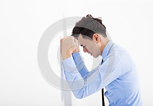 Depressed young business man leaning at the wall in office