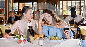 Two young female friends depressed at dinner in a restaurant