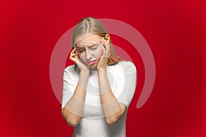 Depressed young girl suffering headache migraine, massaging temples with closed eyes on red studio background