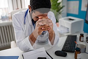 Depressed young male doctor with headache sitting in his office