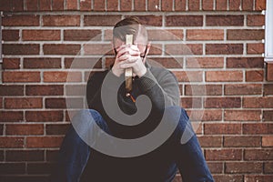 Depressed young male sitting on the ground against a wall holding the Holy Bible