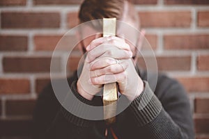 Depressed young male sitting on the ground against a wall holding the Holy Bible