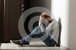 Depressed young man sitting on floor in dark corridor