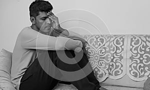 Depressed young man sitting on sofa at home in black and white