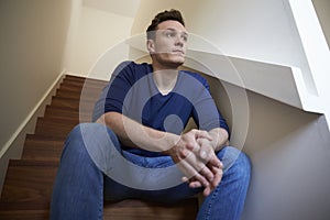 Depressed Young Man Sitting On Stairs At Home