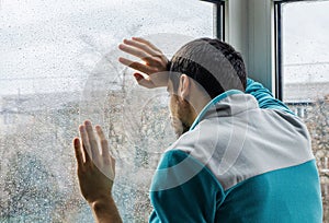 Depressed young man upset with bad news looking through rainy window glass