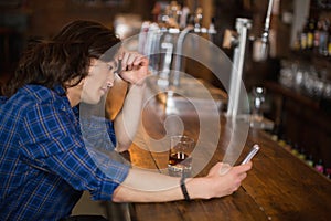 Depressed young man using mobile at pub