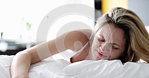 Depressed young woman with alarm clock on bed