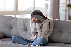 Depressed young woman covering face by hands, crying alone at home