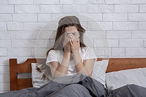 Depressed young woman covering her face and crying on bed at home