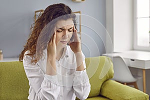 Depressed young woman with headache sitting on sofa