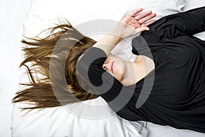 Depressed young woman is lying in her bed, covering her eyes.