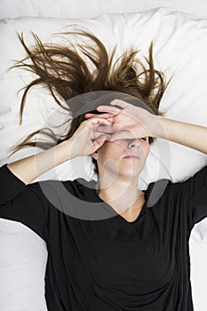 Depressed young woman is lying in her bed, covering her eyes.