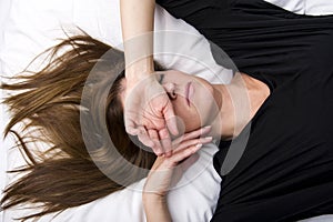 Depressed young woman is lying in her bed, covering her eyes.