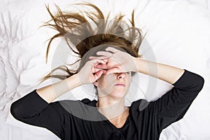 Depressed young woman is lying in her bed, covering her eyes.